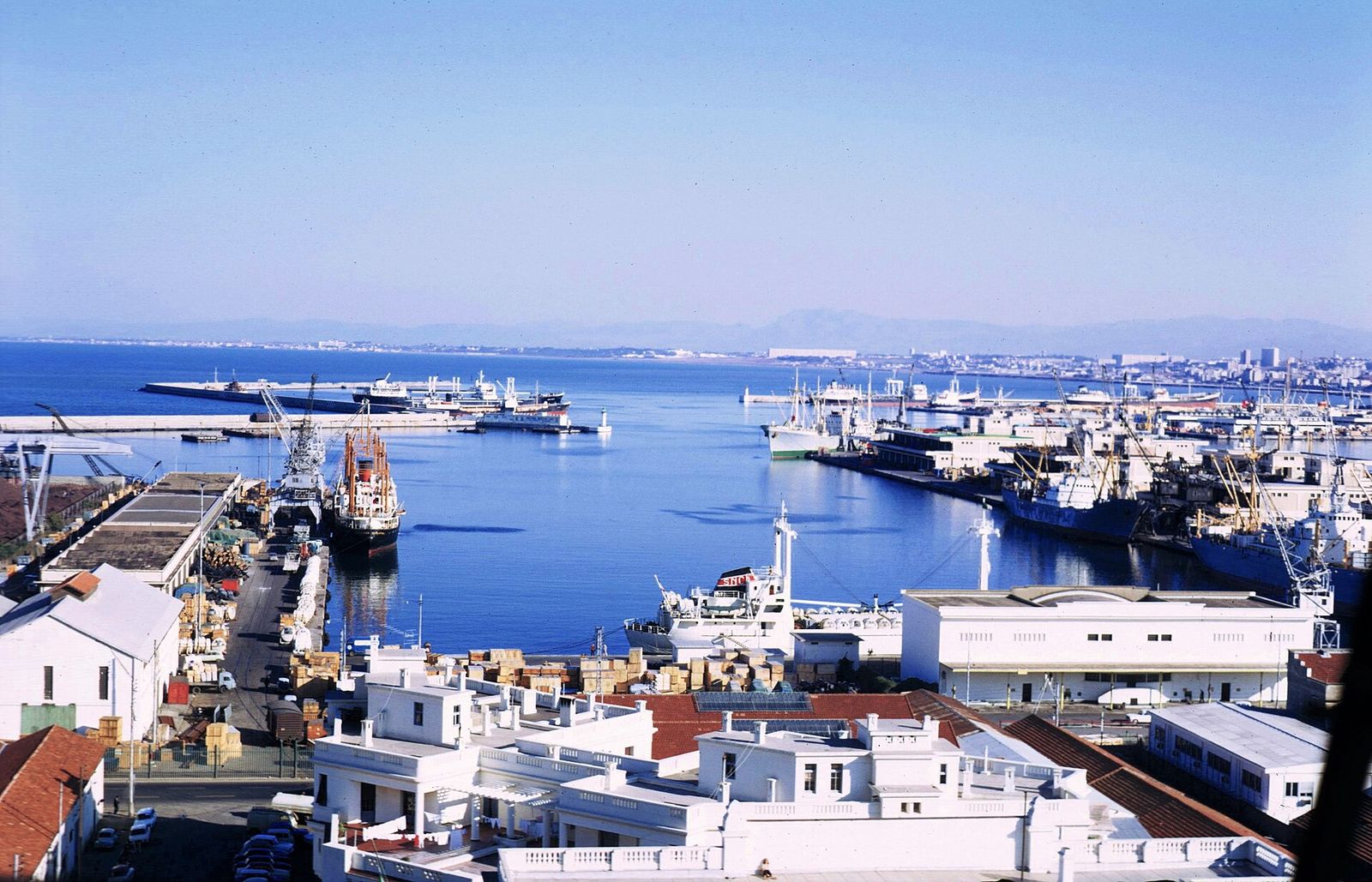 Vue plongeante sur le port d’Alger, ses quais et ses navires sous un ciel bleu