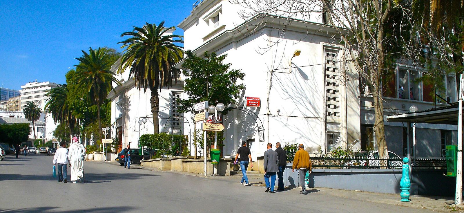 Entrée du centre hospitalo-universitaire Mustapha Pacha à Alger, avec palmiers et passants