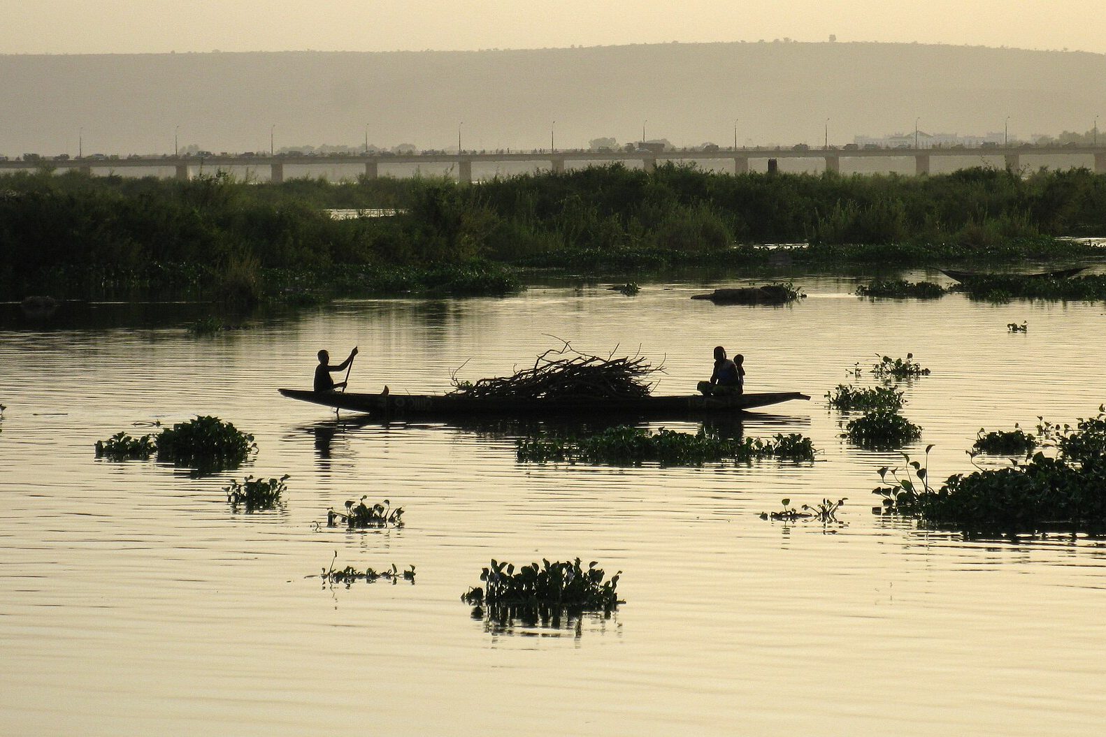 Pirogue sur le fleuve Niger à Bamako au crépuscule, avec le pont Roi-Fahd à l’arrière-plan